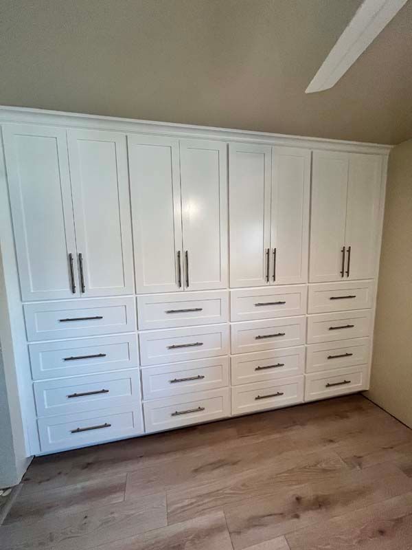 White built-in storage cabinets with drawers and doors; silver hardware, installed against beige walls and wood-look flooring.