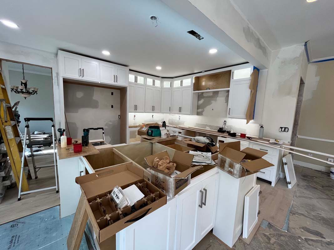 Kitchen renovation in progress, with white cabinets, island, and construction materials scattered throughout.