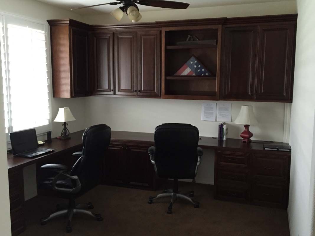 Home office with dark wood cabinets, two desks, black office chairs, and a laptop.