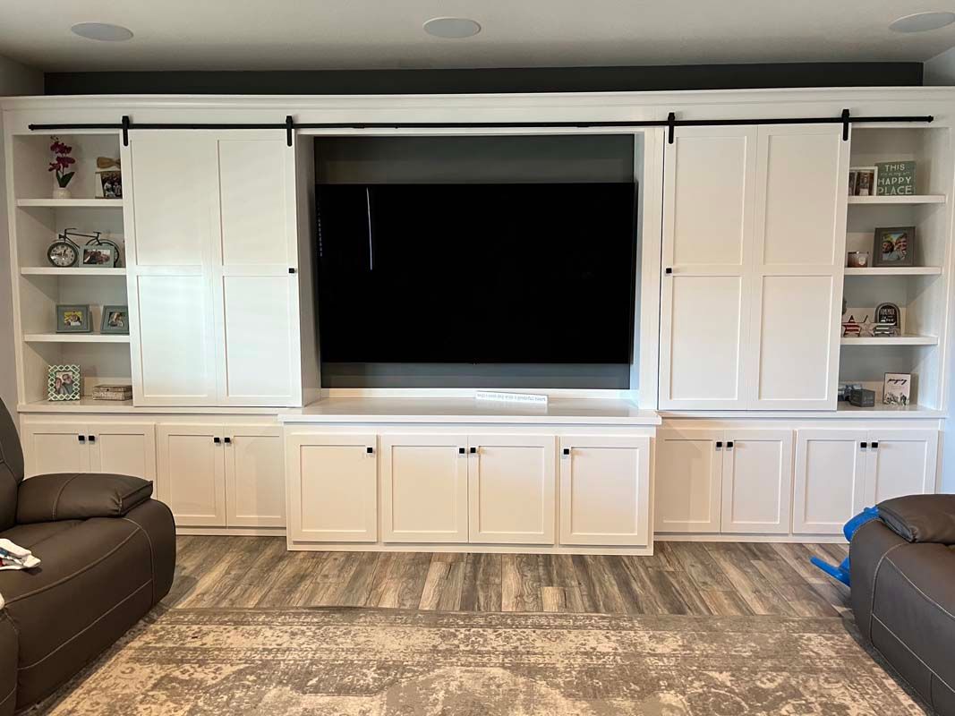 White entertainment center with sliding doors, built-in shelves, and a large TV in a living room.