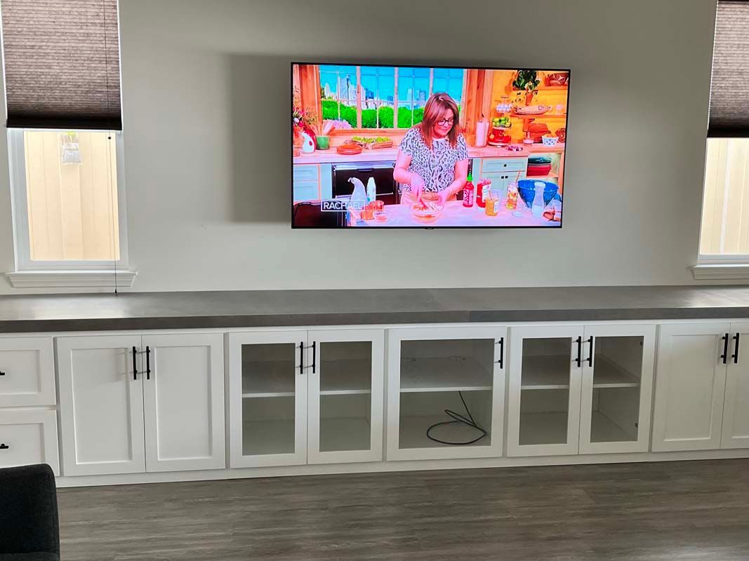 White cabinets with glass doors below a wall-mounted TV displaying a cooking show.