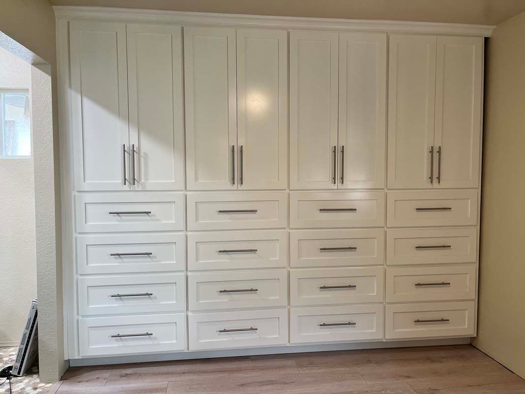 White built-in storage cabinets with drawers and doors in a room with light-colored walls and flooring.