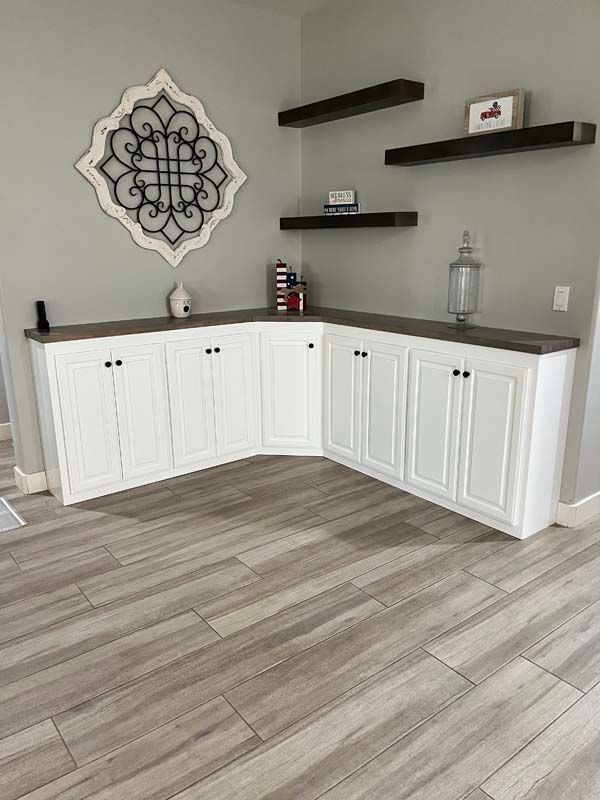 White cabinets with dark countertop in corner of room, with floating shelves above.