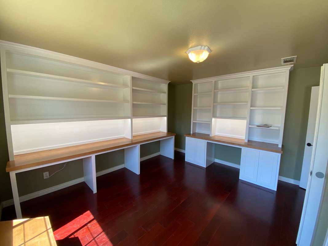 Two built-in white bookshelves with desks on either side of a room, wooden floor, and olive green walls.