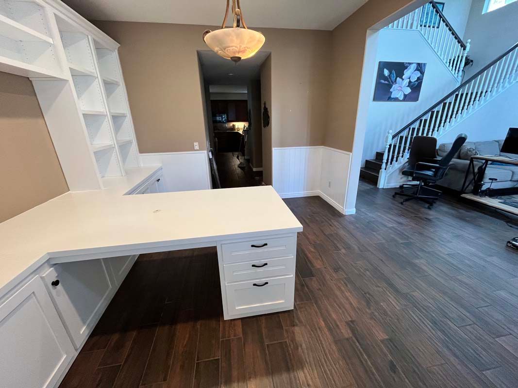 White desk with shelving, dark wood floors, and a staircase in a home.