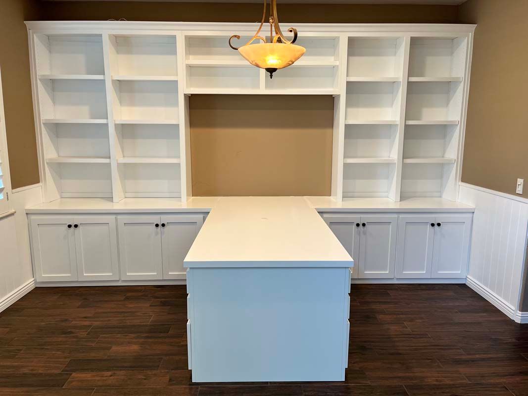 White built-in bookshelves and cabinets with a central desk in a room with hardwood floors.