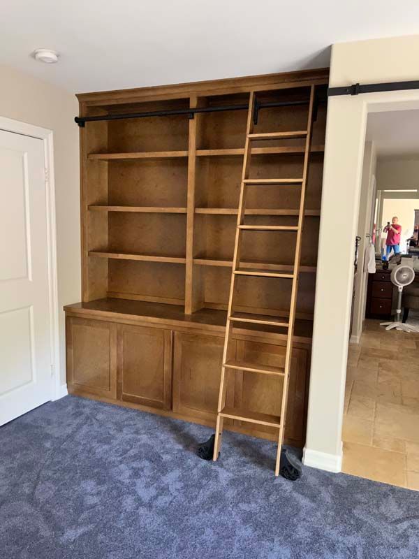 Wooden bookshelf with rolling ladder against a light-colored wall.