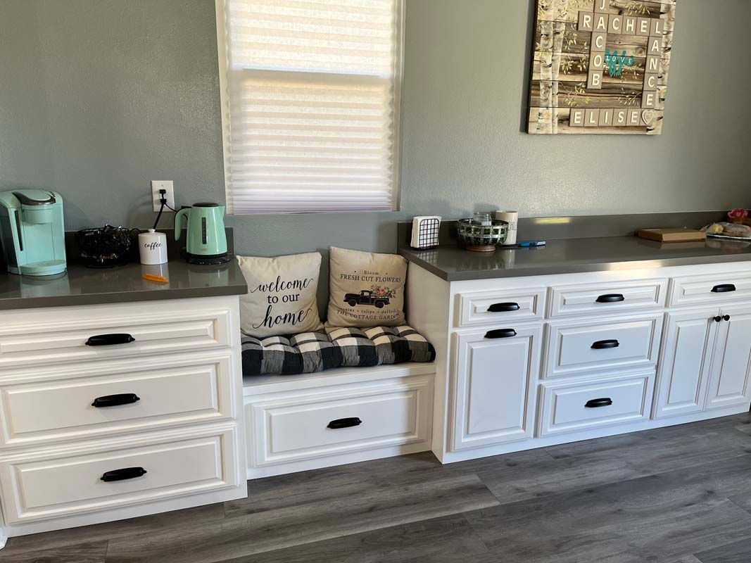 Kitchen with white cabinets, gray countertops, and a window seat with pillows.