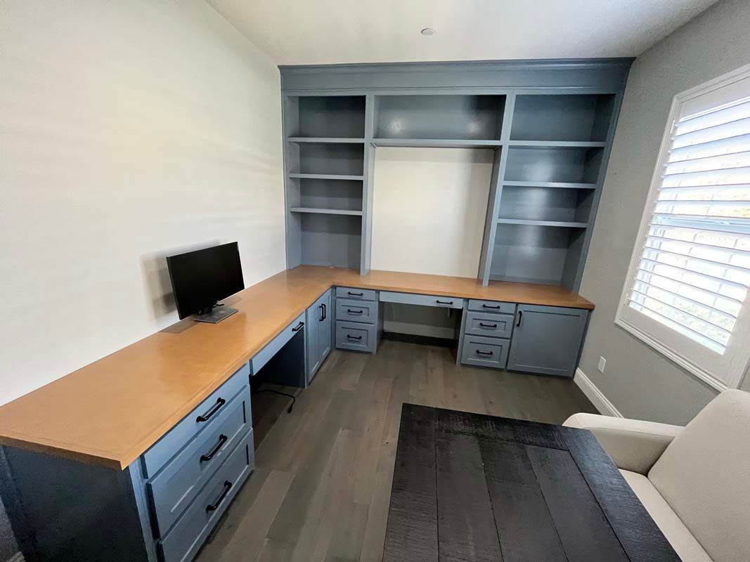 Built-in blue desk with bookshelves in a home office. Includes a computer monitor and a window with blinds.