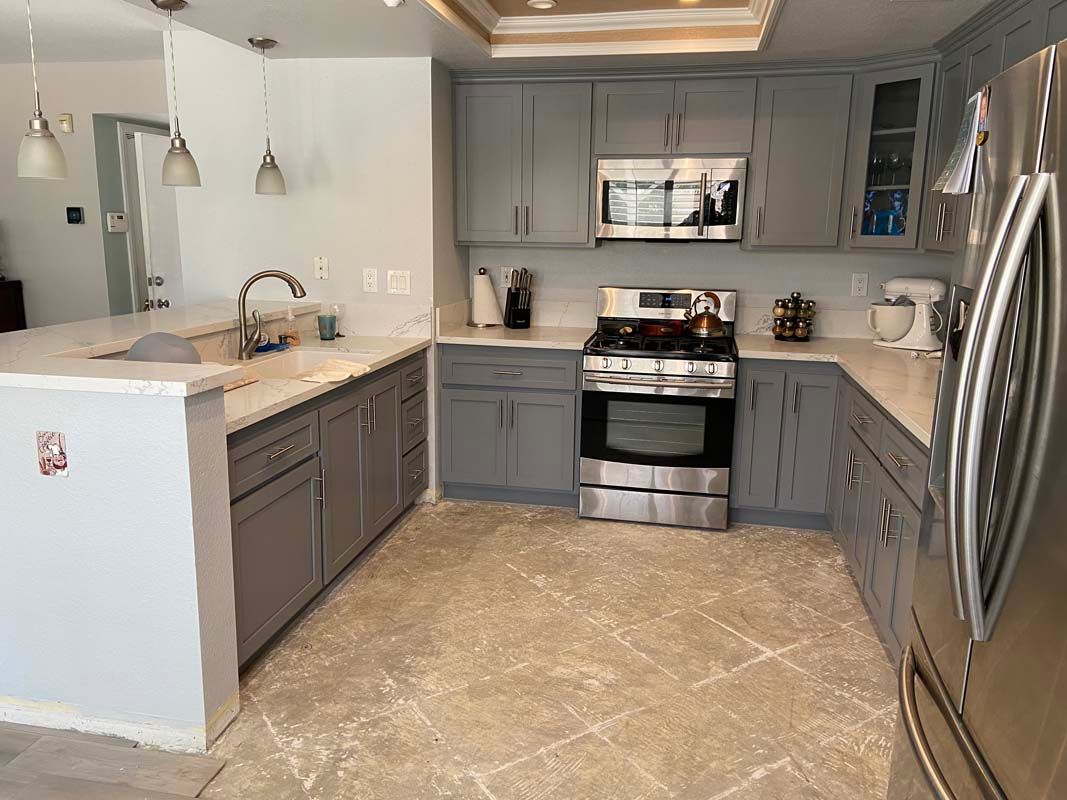 Gray kitchen with white countertops, stainless steel appliances, and beige tile floor.