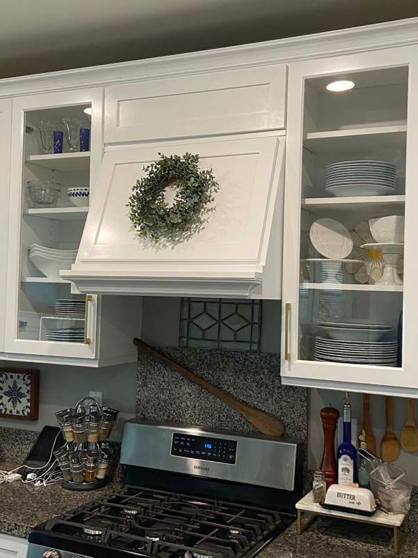 White kitchen cabinets with glass doors, a decorative wreath, and stainless steel range.