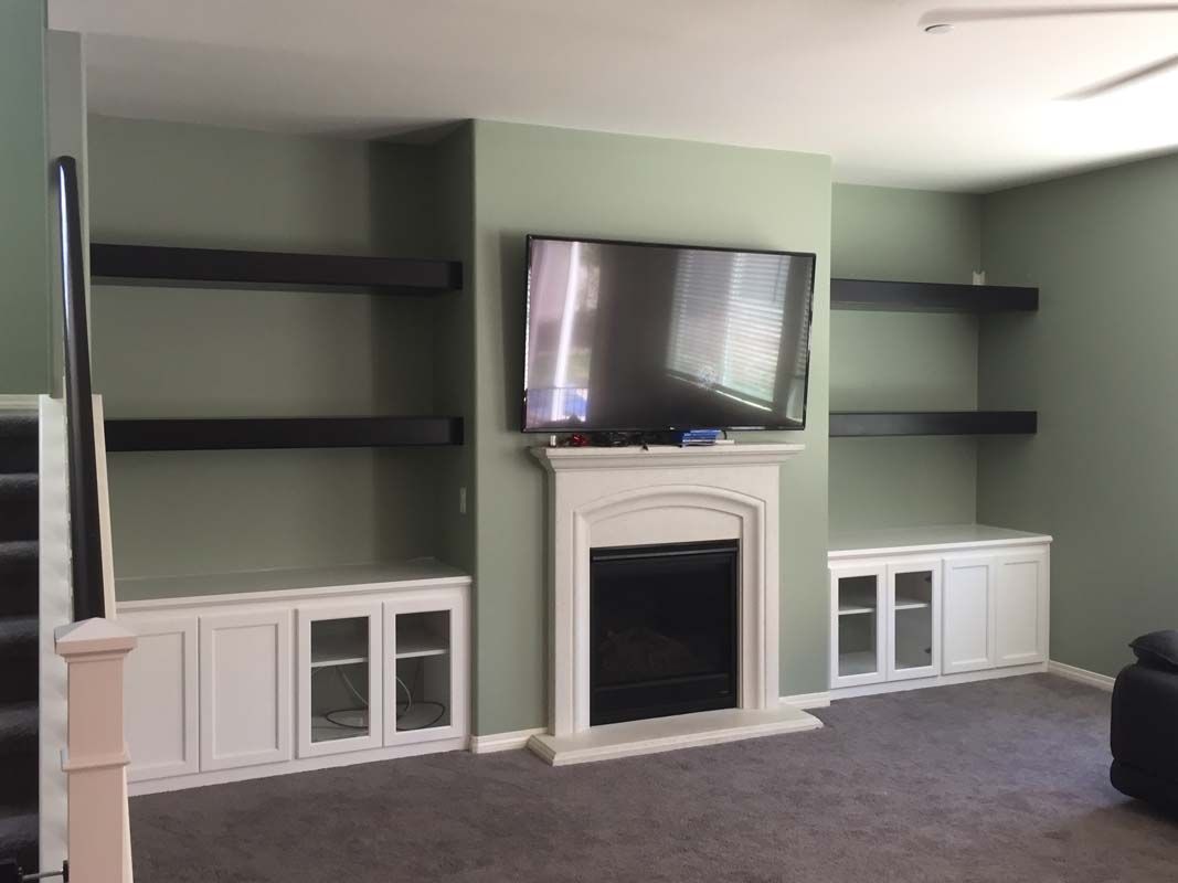 Living room with fireplace, TV, built-in white cabinets, and black shelves against a sage green wall.