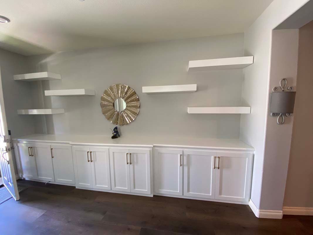 White built-in cabinets and shelves on a gray wall, a gold mirror, and a wall lamp, with wood flooring.