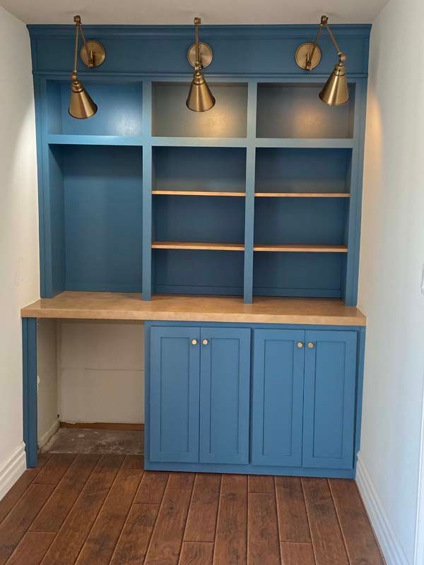 Built-in blue desk with shelves and cabinets, wood countertop and floor, gold sconce lights.