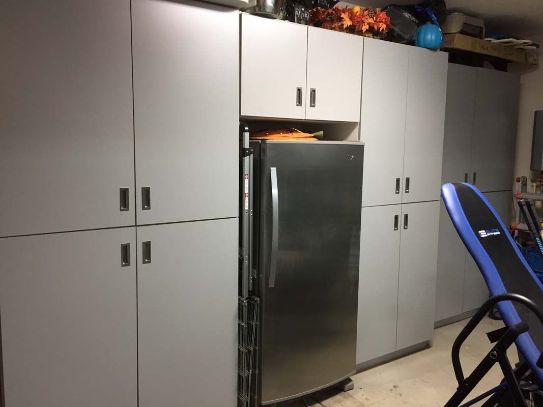 Garage with gray cabinets, a stainless steel refrigerator, and an exercise machine.