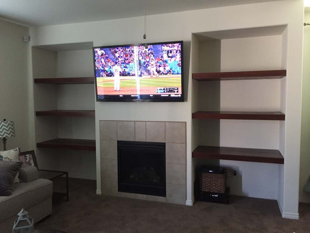 Living room with a fireplace, TV, and built-in shelves. Dark shelves, beige wall, TV is on.
