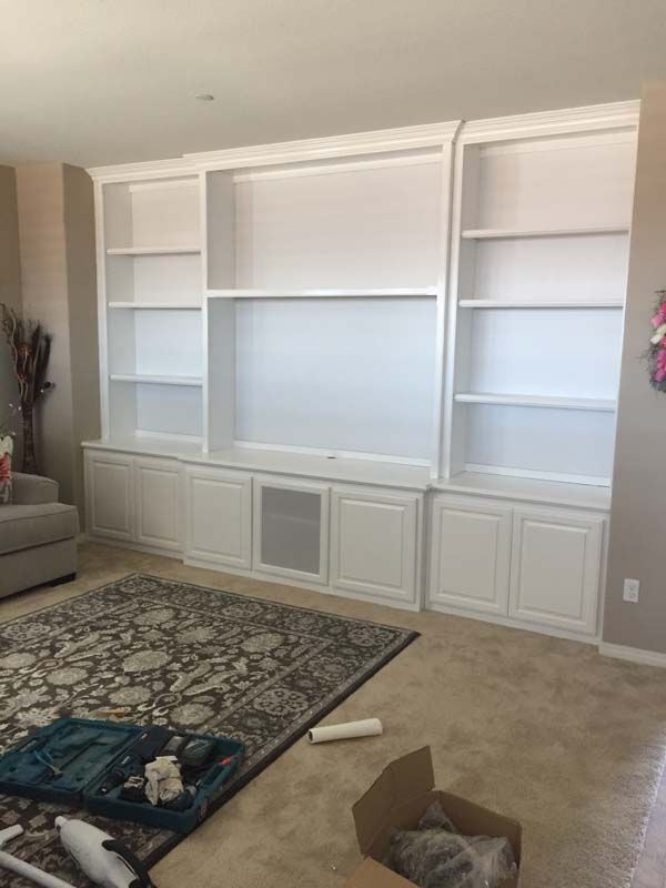 White built-in cabinet with shelves and doors against a wall. A rug and tools are in front.