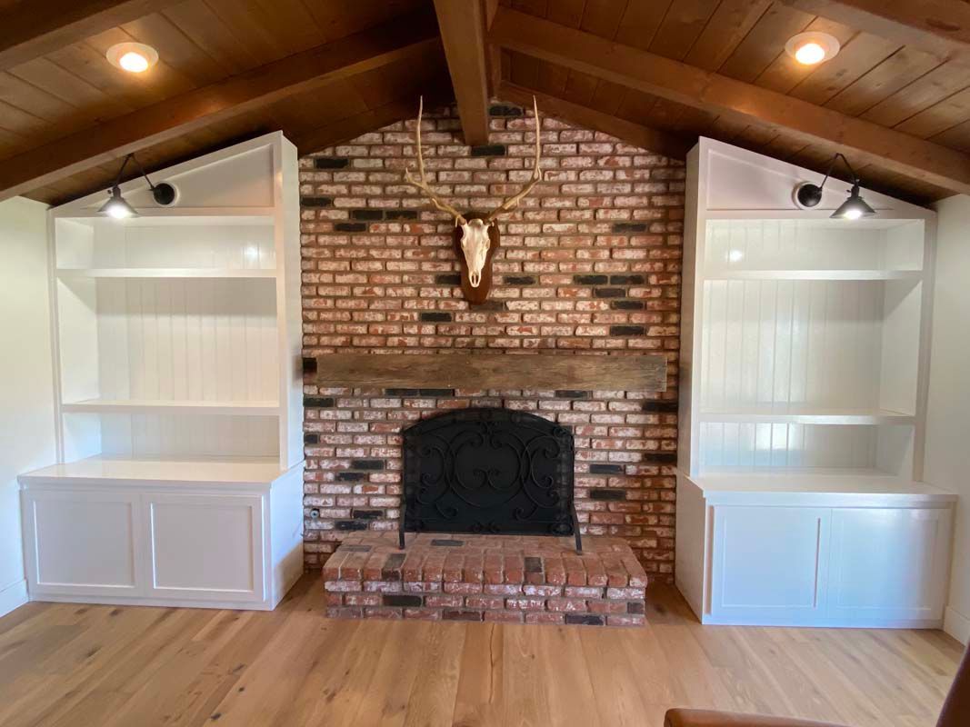 Fireplace flanked by white bookshelves in a room with wood flooring, and exposed brick.