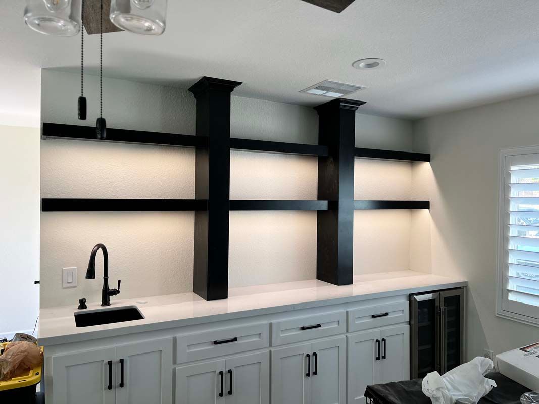 Black and white home bar with built-in shelves, cabinetry, countertop, sink, and wine cooler.