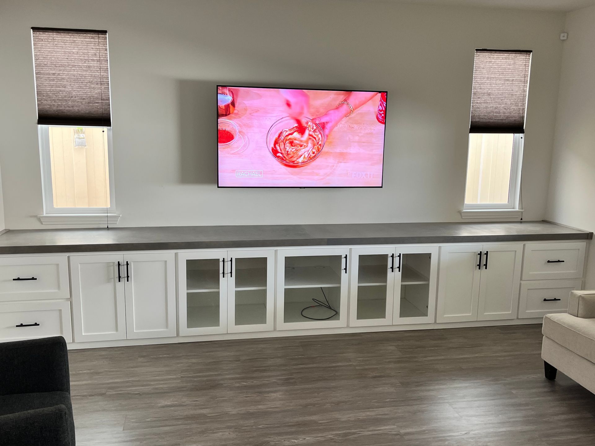 Built-in white cabinets with a TV above, flanked by windows with blinds, against a white wall.
