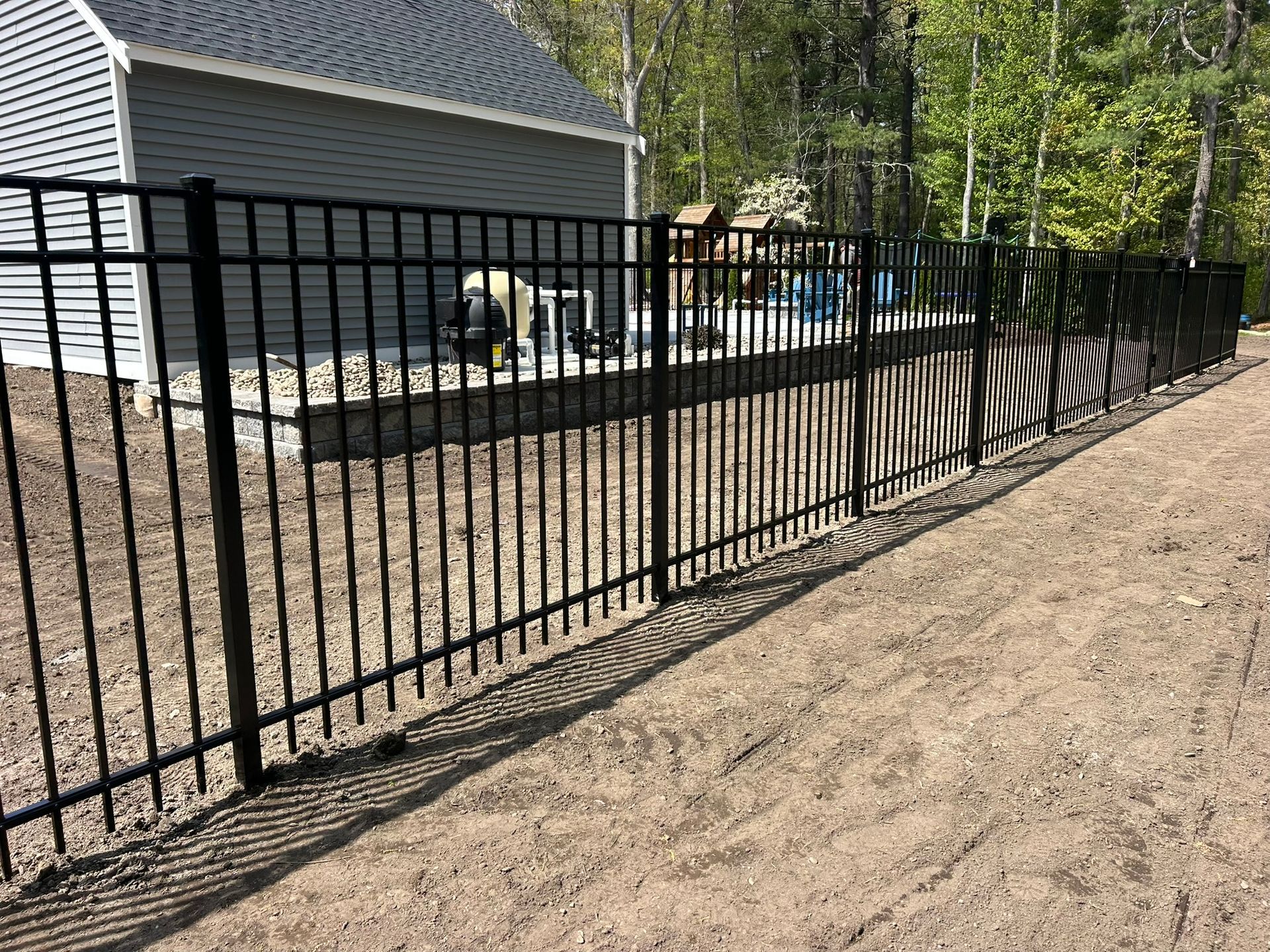 Black metal fence lining a gravel yard beside a gray house and trees