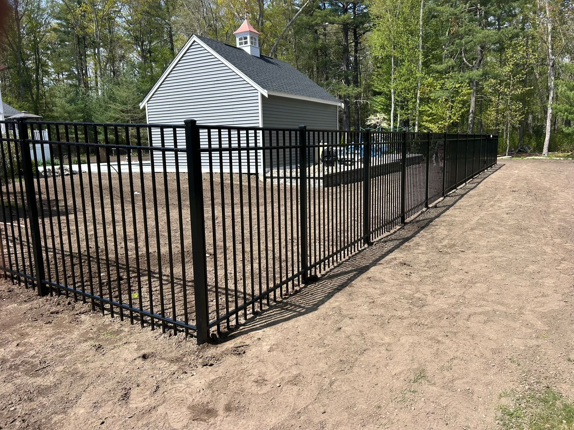 Black metal fence around a small white building in a wooded outdoor area.