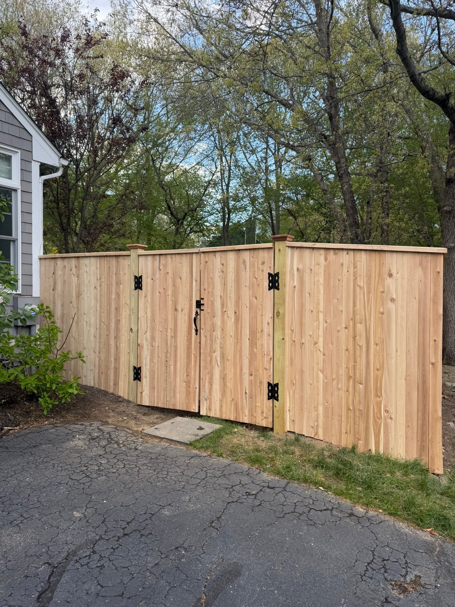 Wooden double gate and privacy fence beside a gravel driveway under trees