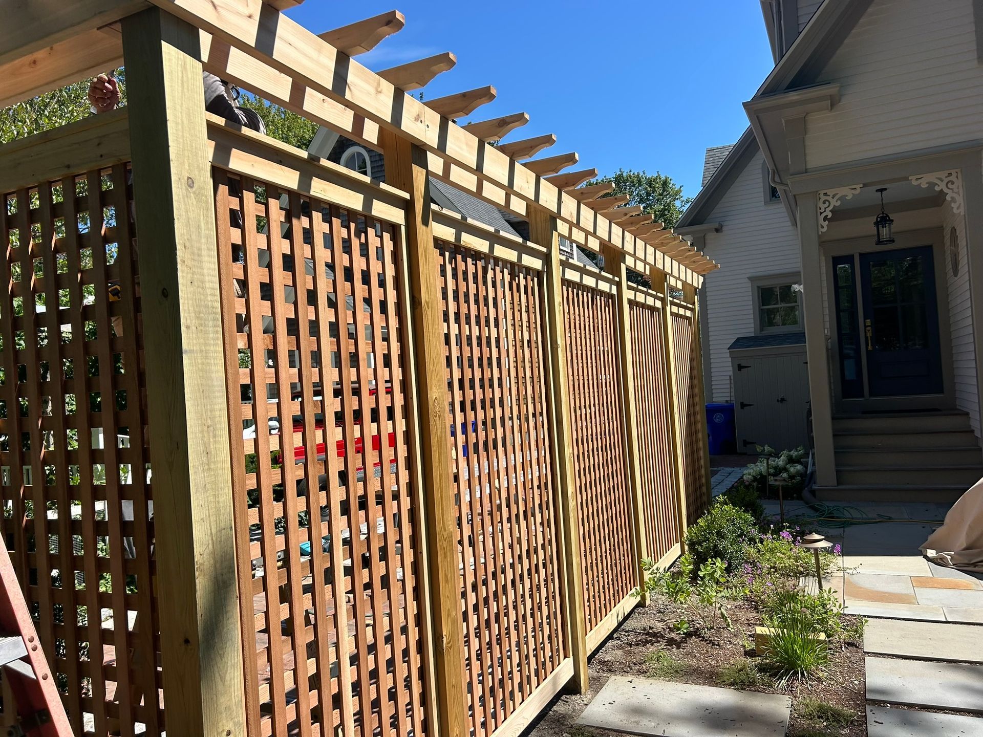 Wooden lattice fence and gate beside a house courtyard with a stone path and greenery
