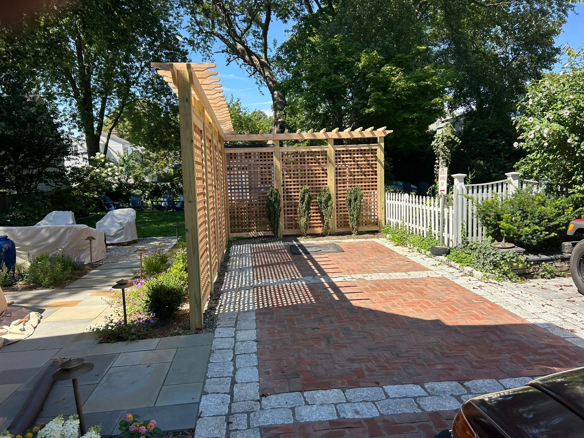 Backyard patio with brick and stone walkway leading to a wooden pergola and garden fence
