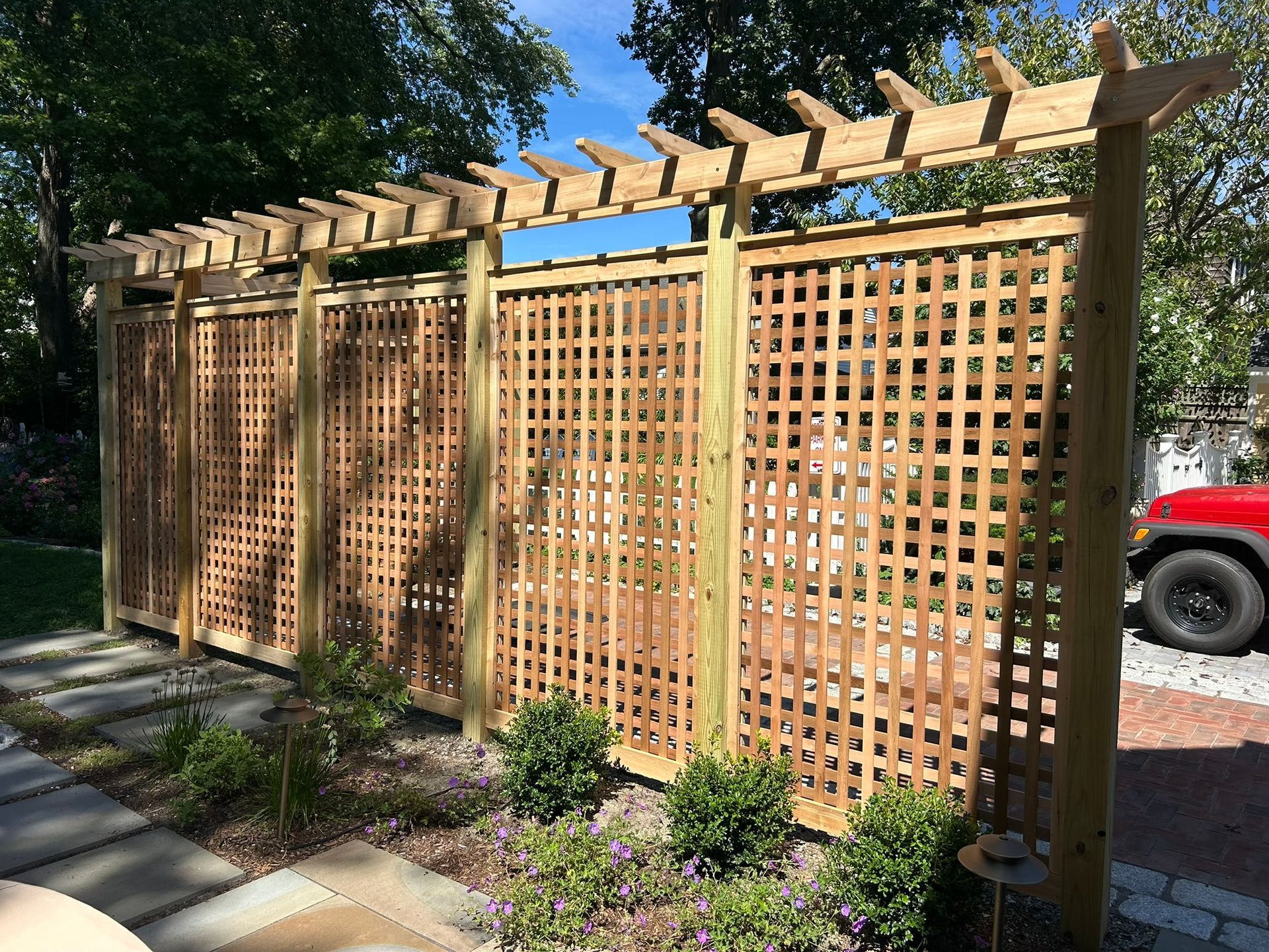 Wooden lattice privacy screen with pergola in a landscaped yard, beside a sidewalk and trees