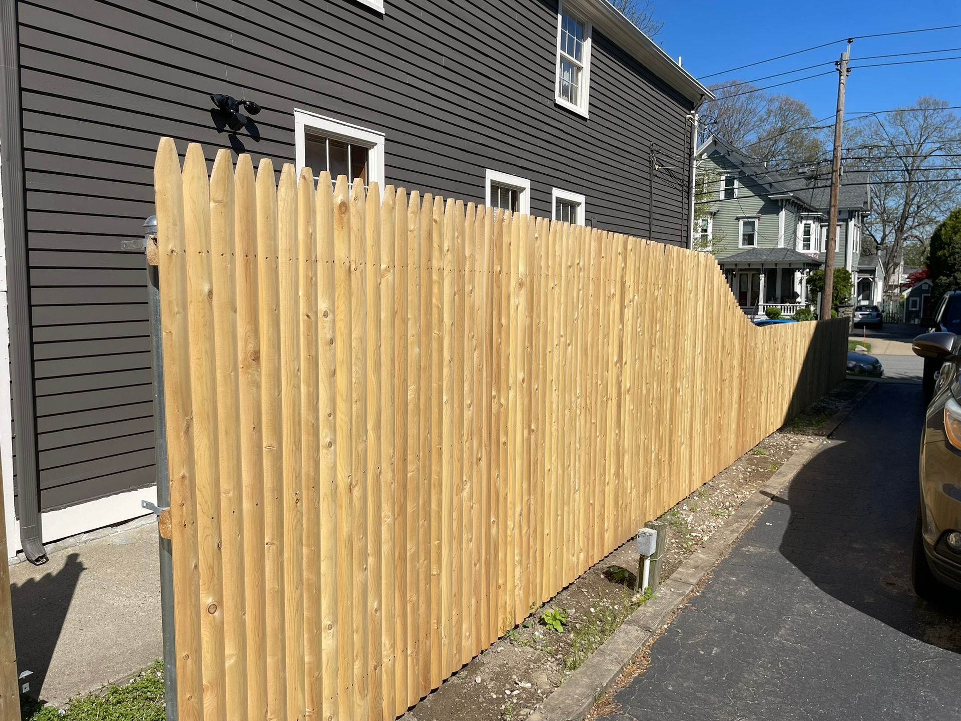 Tall wooden privacy fence beside a gray house along a narrow street
