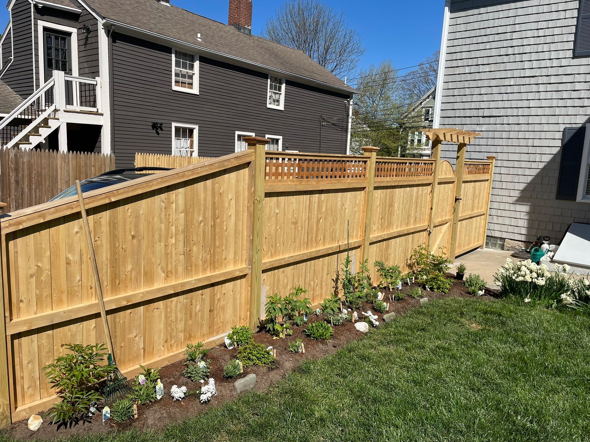 Backyard with new wooden fence, flower bed, and green lawn beside two houses