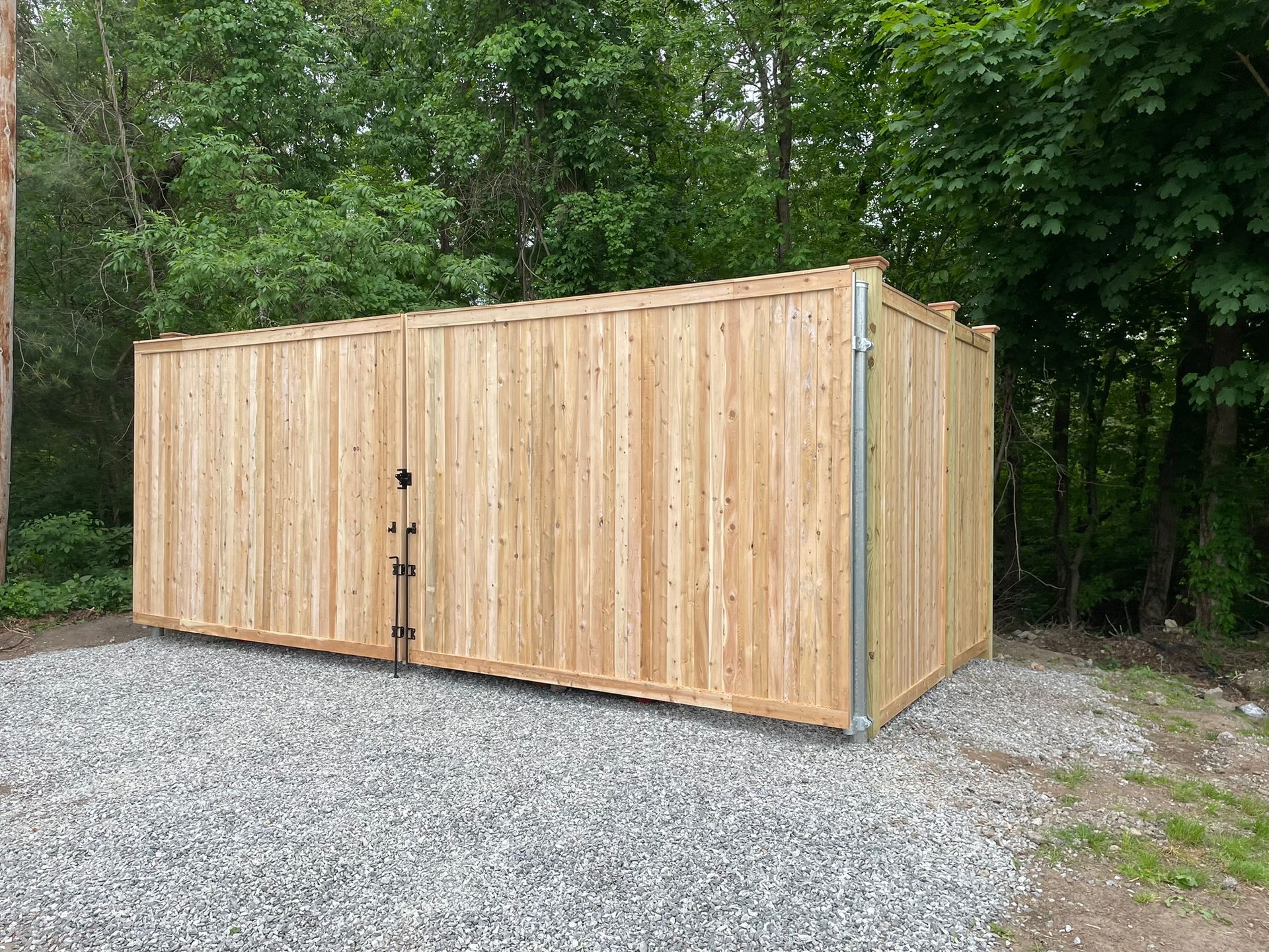 Wooden storage shed on a gravel lot, surrounded by green trees.