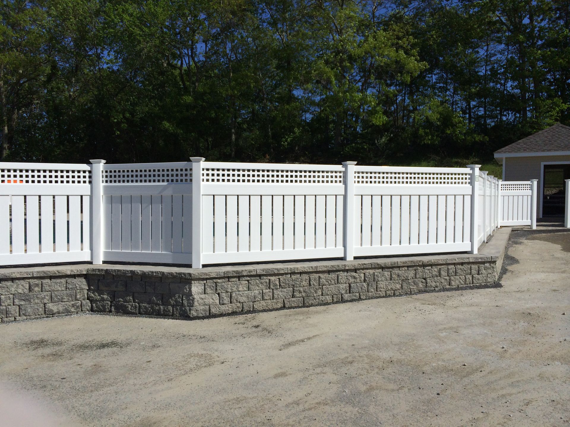 A white fence with a stone wall in front of a house.