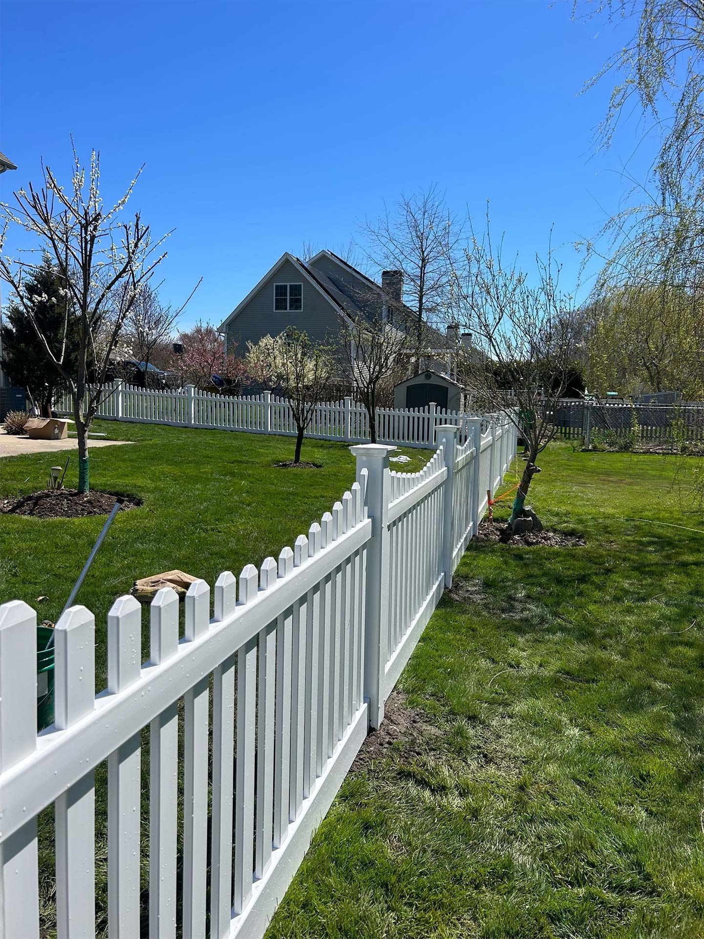 A white picket fence surrounds a lush green yard in front of a house.
