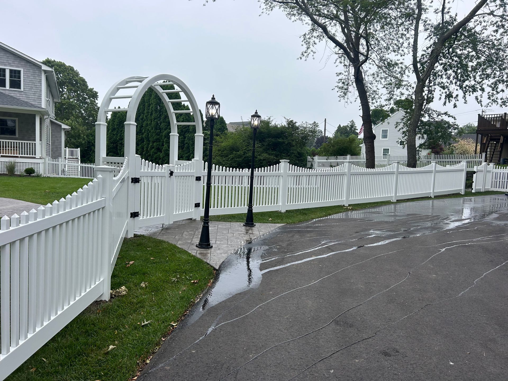 A white picket fence surrounds a driveway and a house.