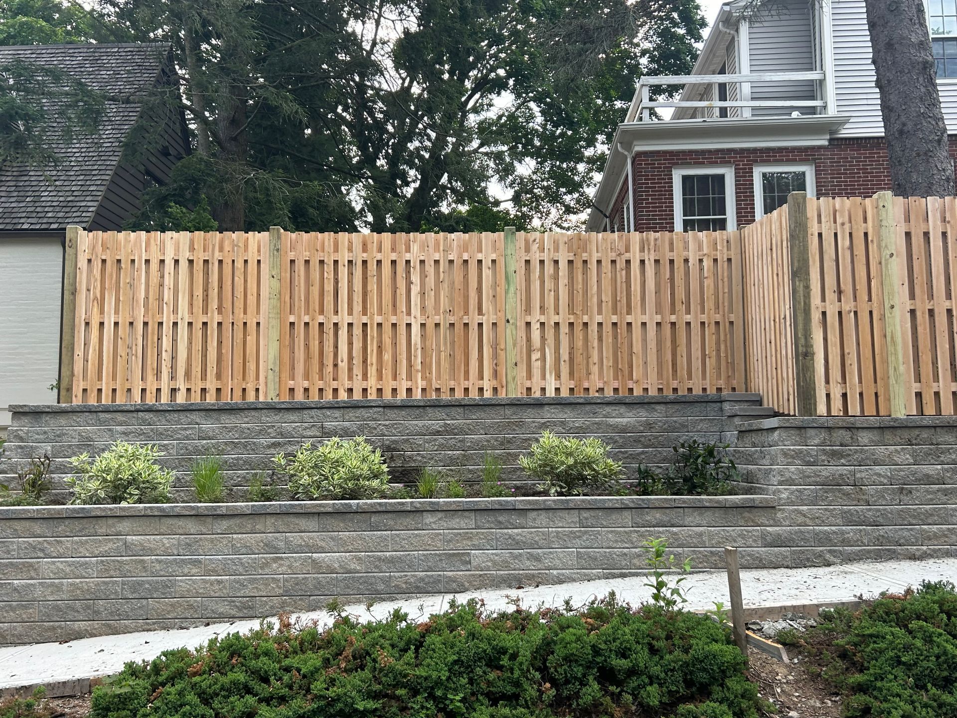A wooden fence surrounds a stone wall in front of a house