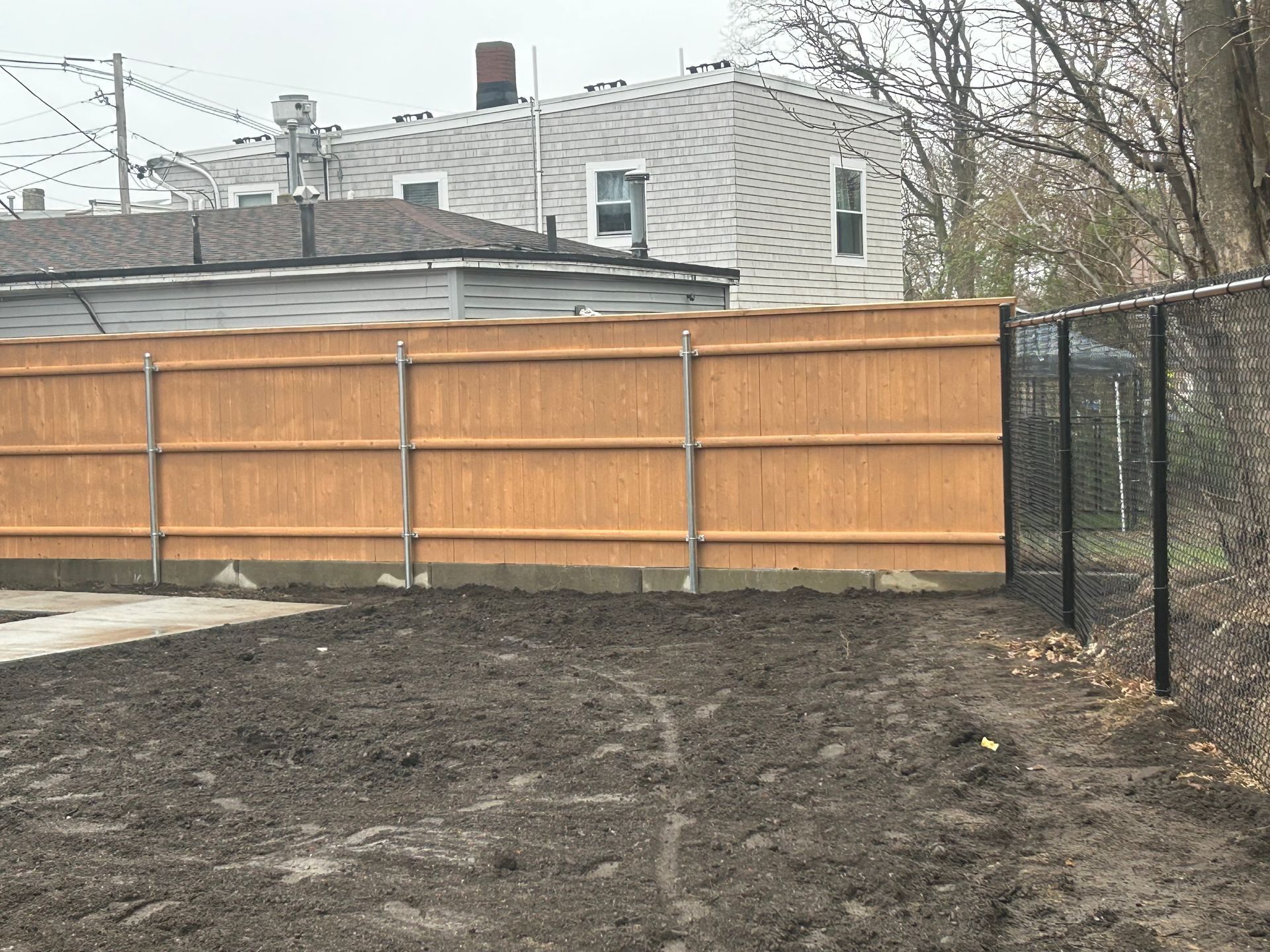 A wooden fence is surrounding a dirt yard in front of a house.