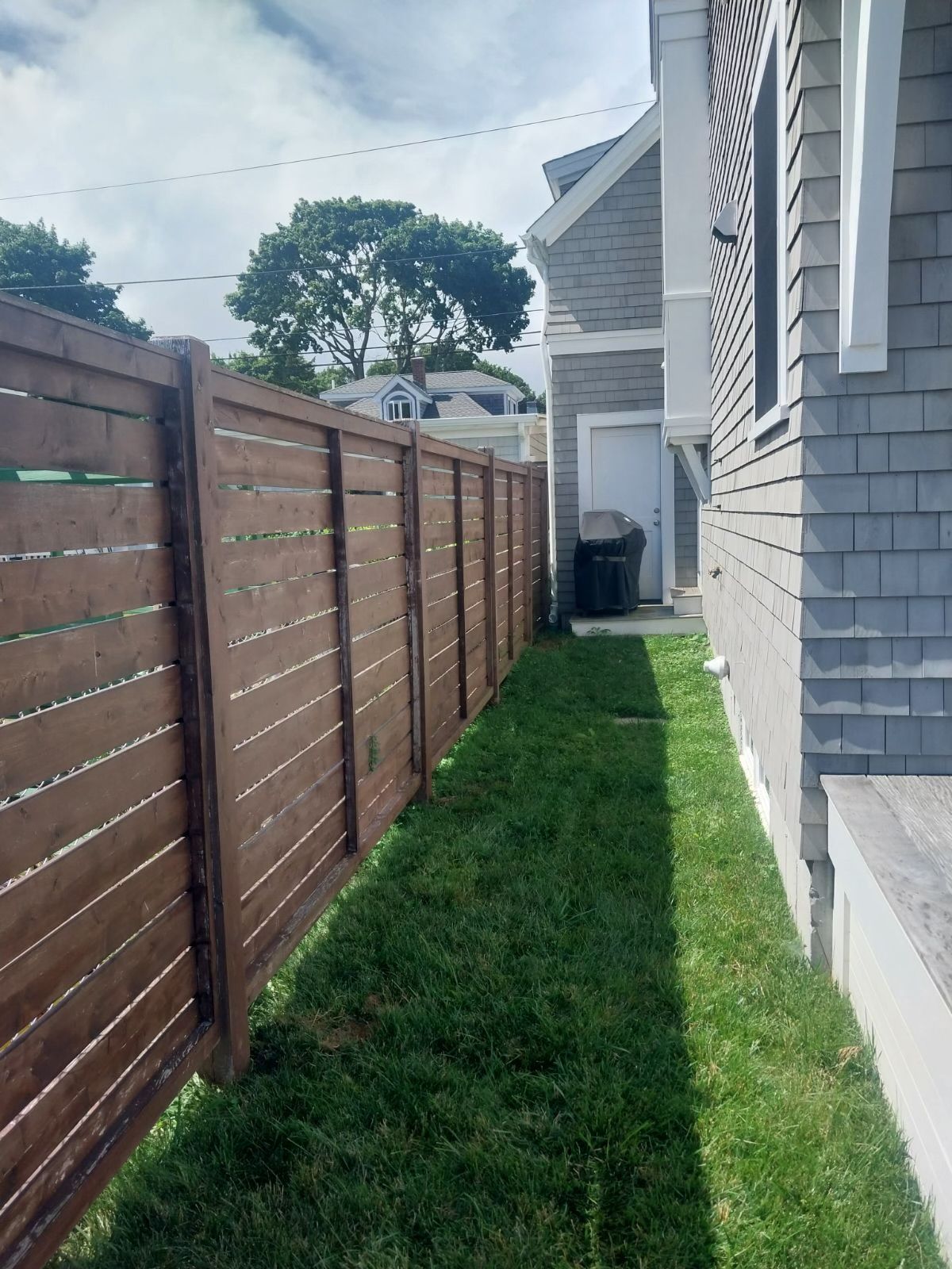 A wooden fence surrounds a lush green yard next to a house.