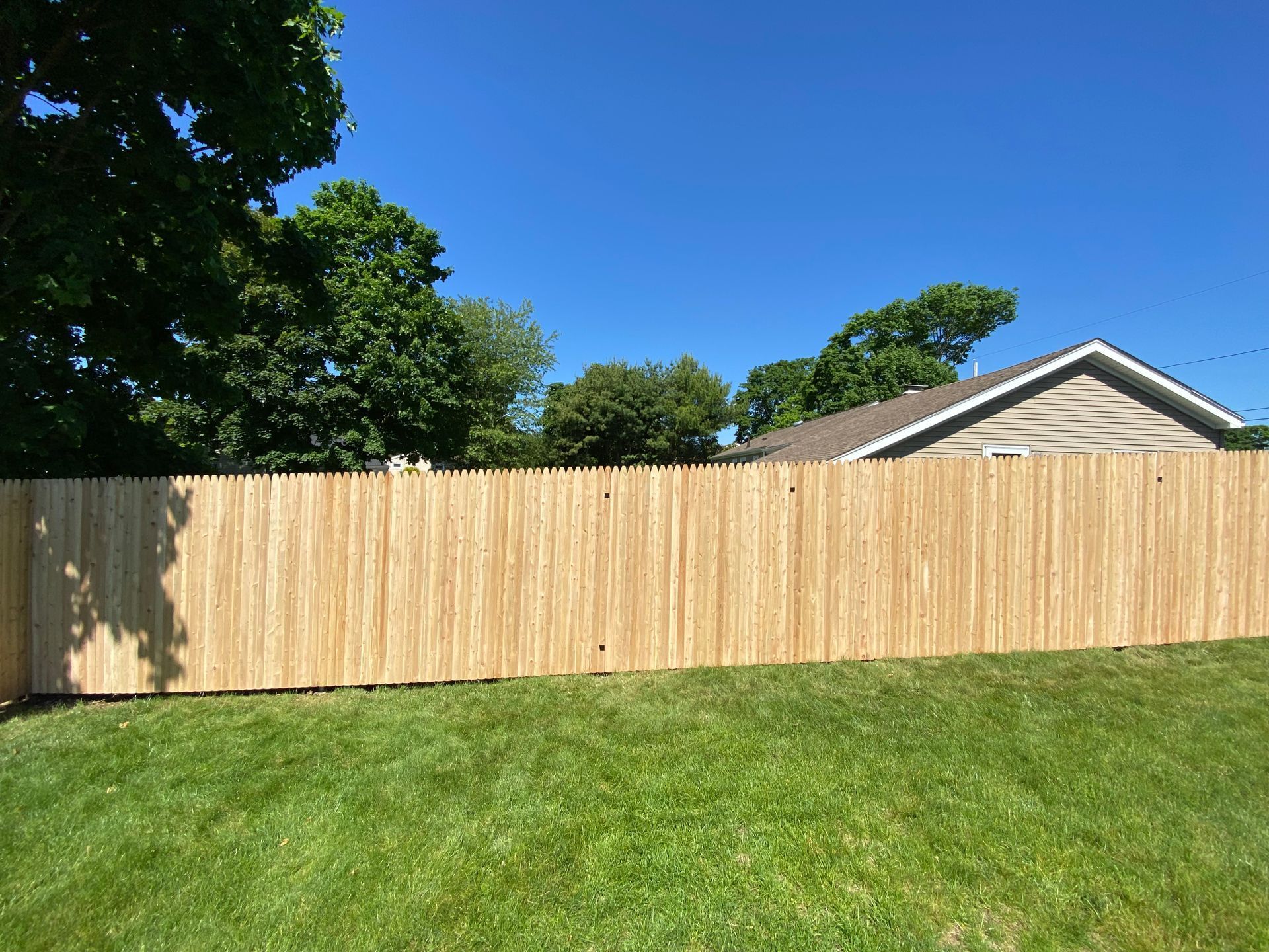 A wooden fence surrounds a lush green lawn in front of a house.