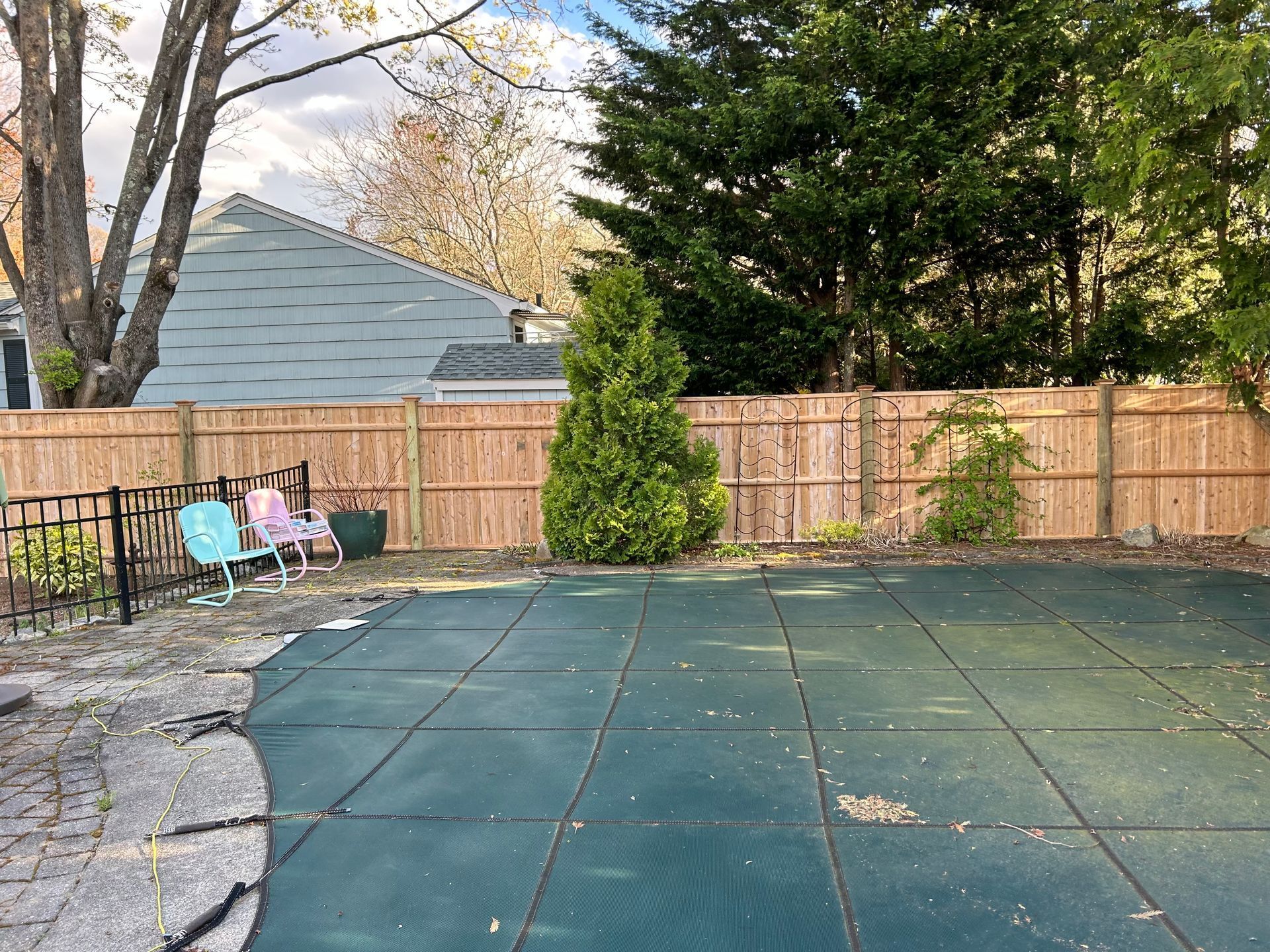 A wooden fence surrounds a swimming pool with a green cover.
