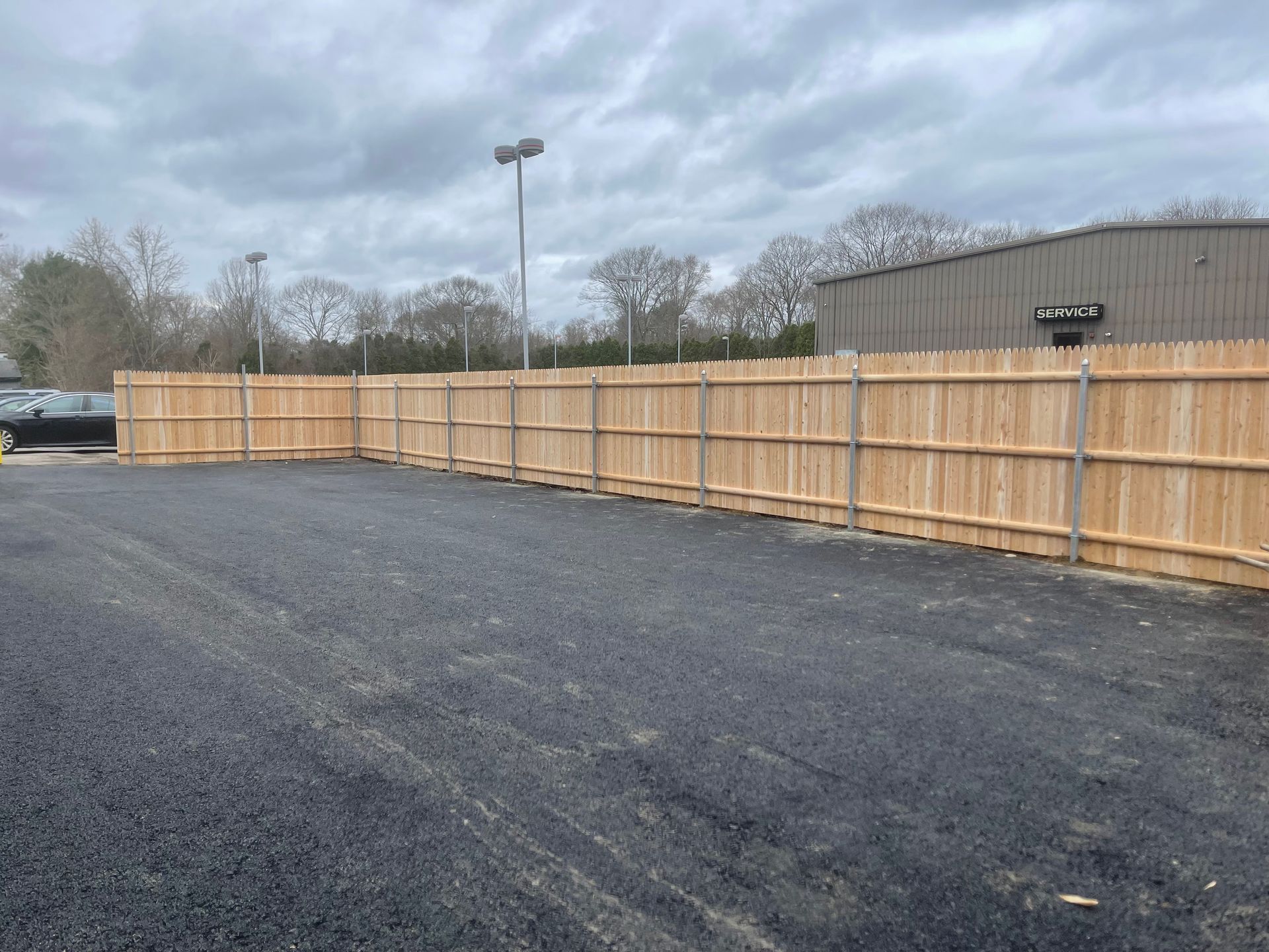 A wooden fence surrounds a parking lot with a building in the background