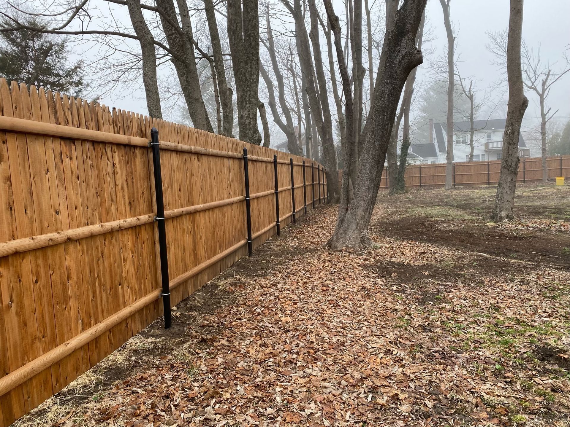 A wooden fence is surrounded by trees and leaves in a field.