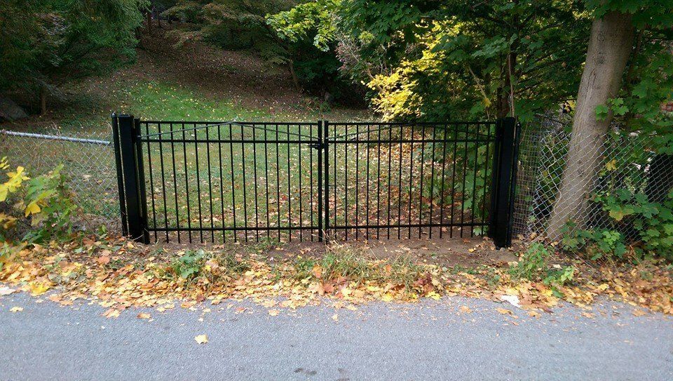 A black gate is sitting on the side of a road next to a tree.