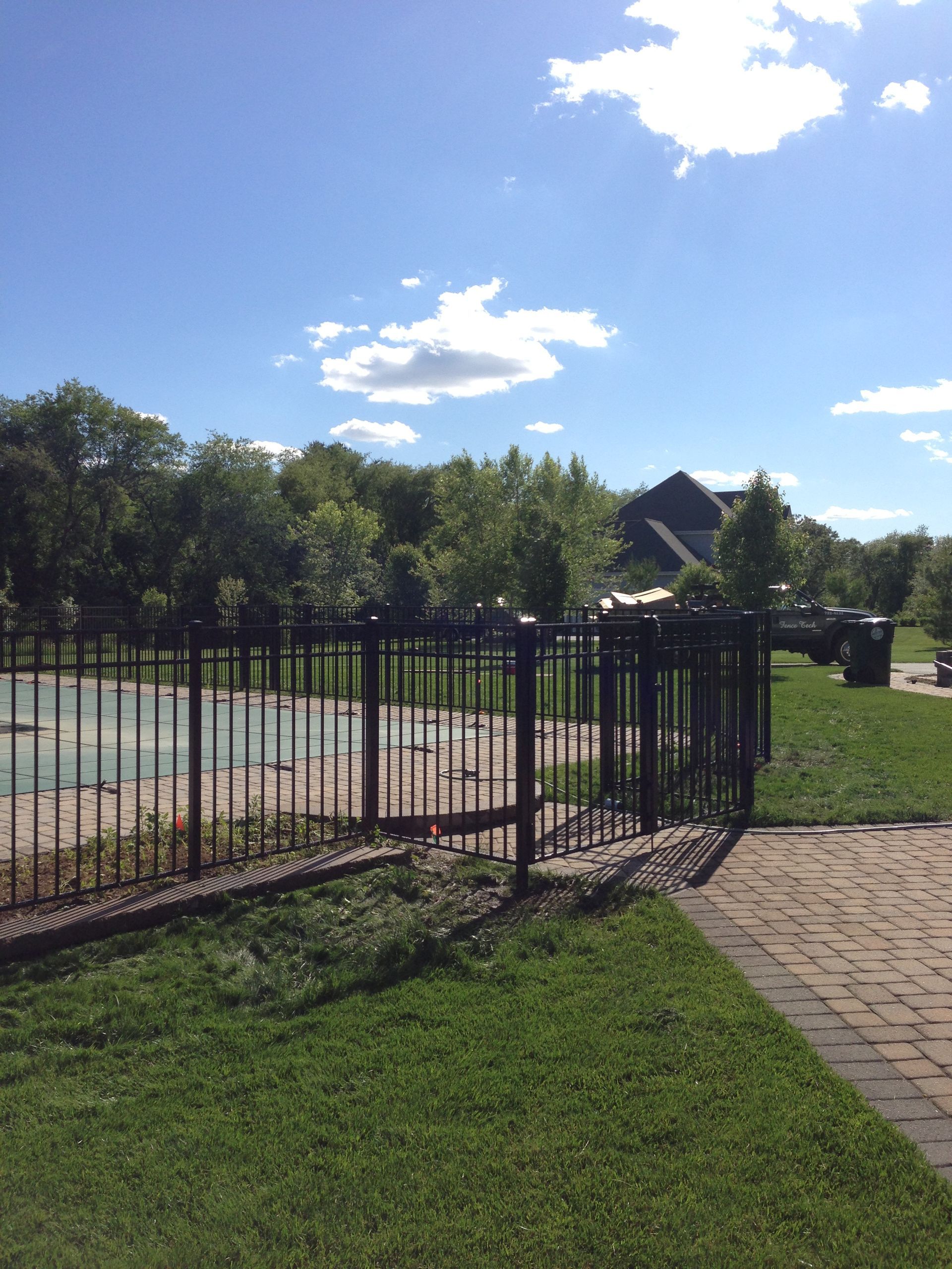 A fence surrounds a swimming pool with a house in the background