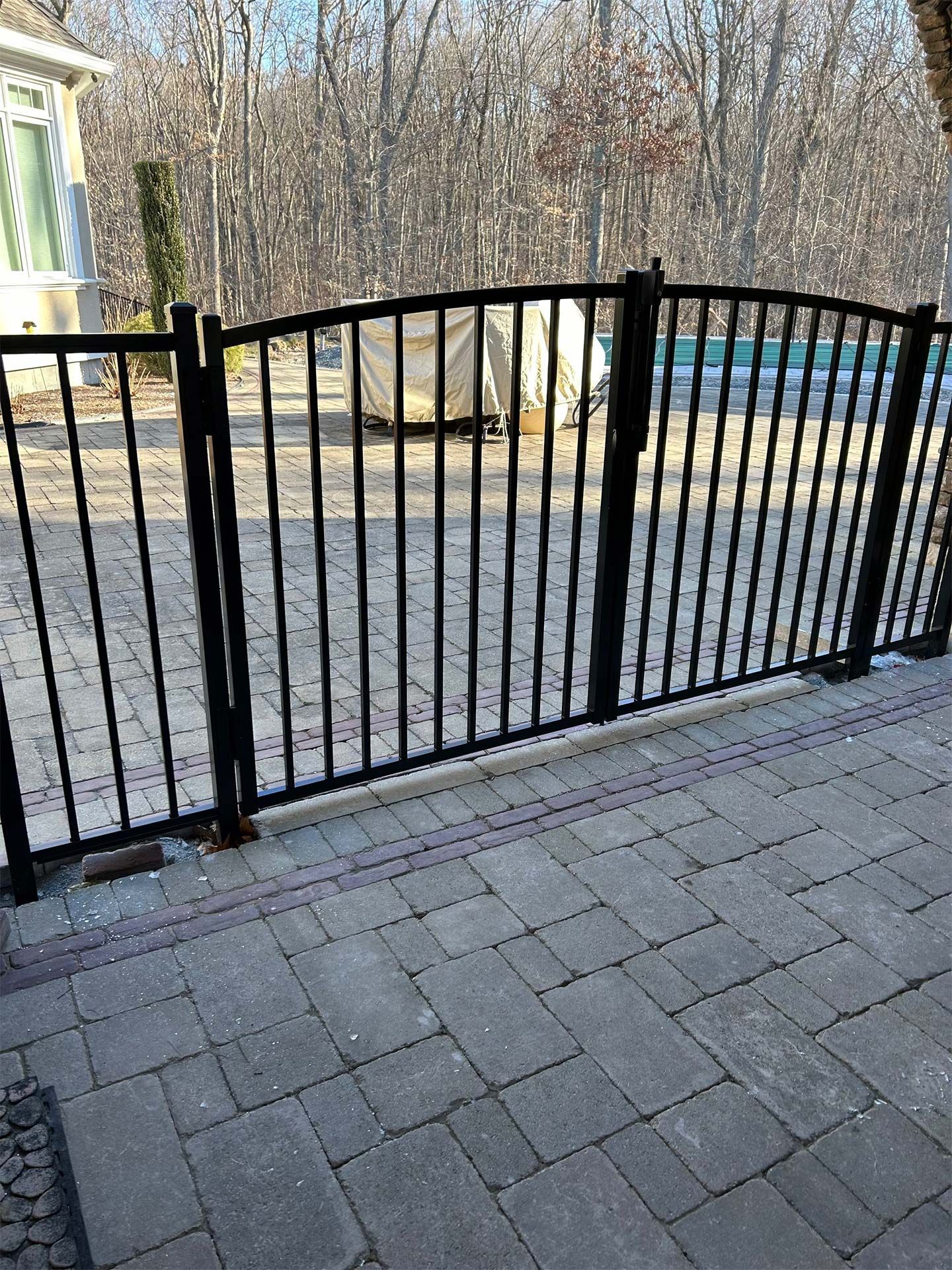 A black metal fence is surrounding a brick walkway.