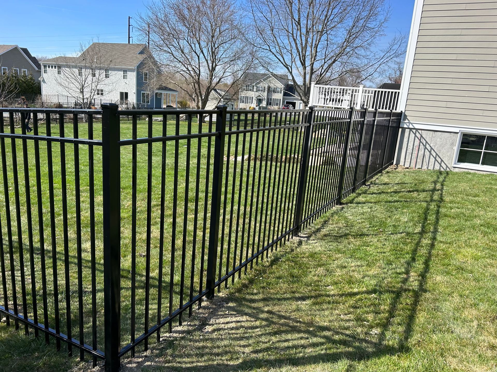 A black metal fence surrounds a lush green field in front of a house.