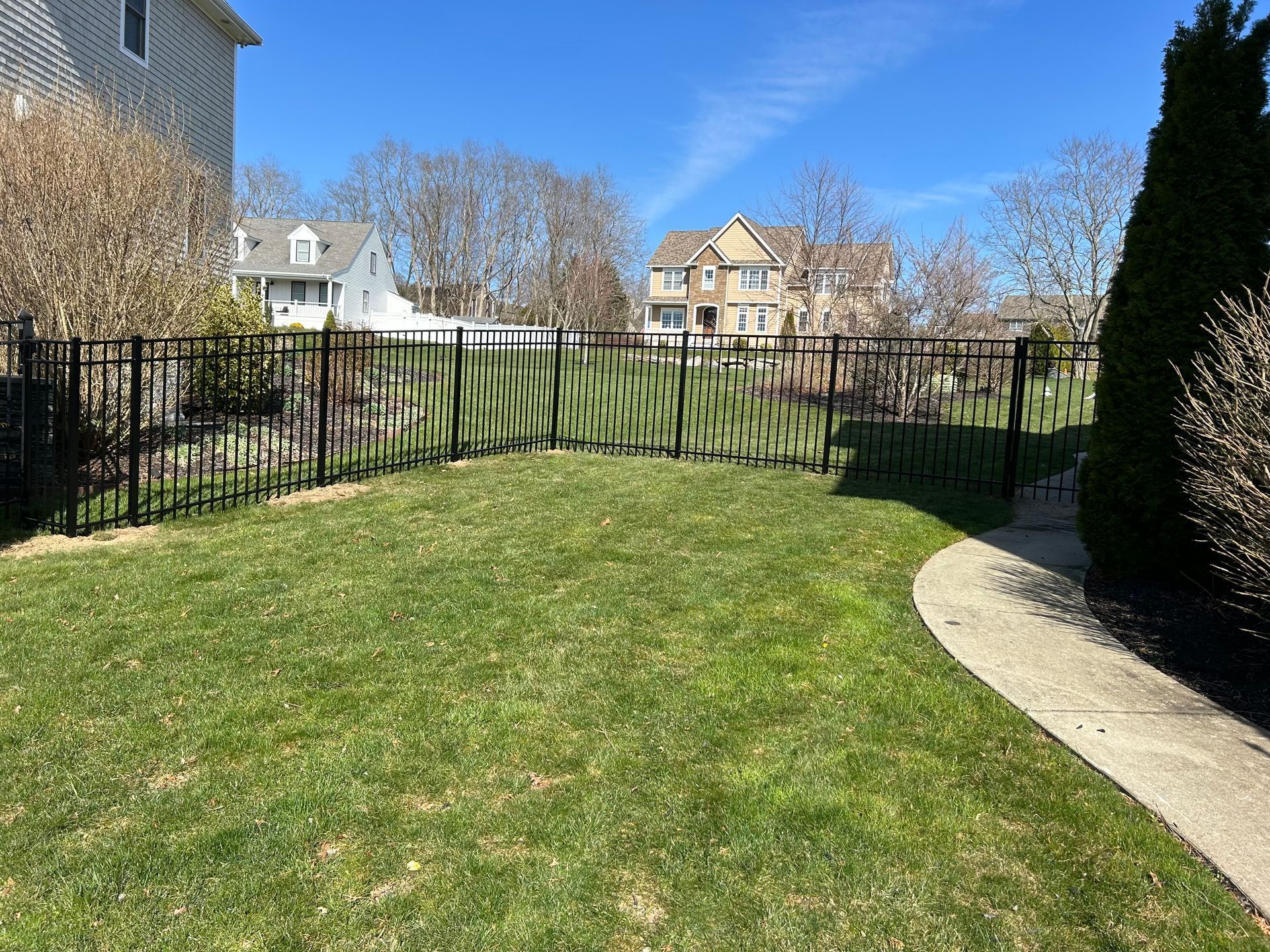 A backyard with a fence and a walkway leading to a house.
