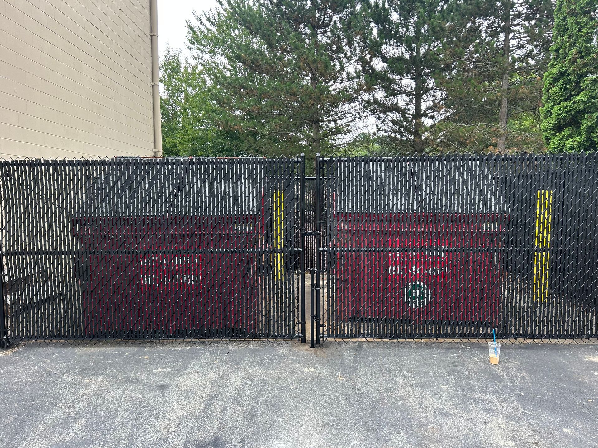 A red dumpster is behind a black fence.