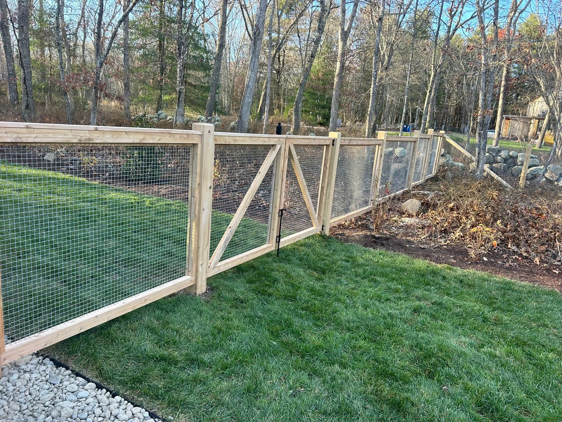 Wooden garden fence with wire mesh and a gate beside a grassy yard and leaf-covered path in autumn